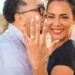 Close-up of a happy couple showing off an engagement ring outdoors.