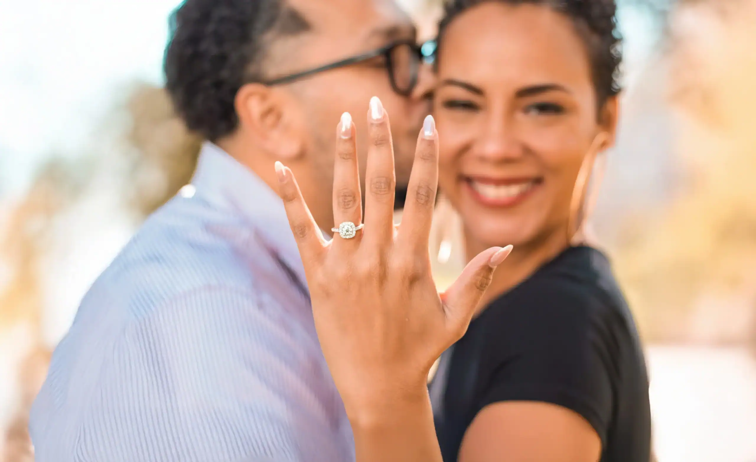 Close-up of a happy couple showing off an engagement ring outdoors.