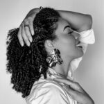 Elegant woman with curly hair smiling, showcasing beauty and confidence in a black-and-white portrai.