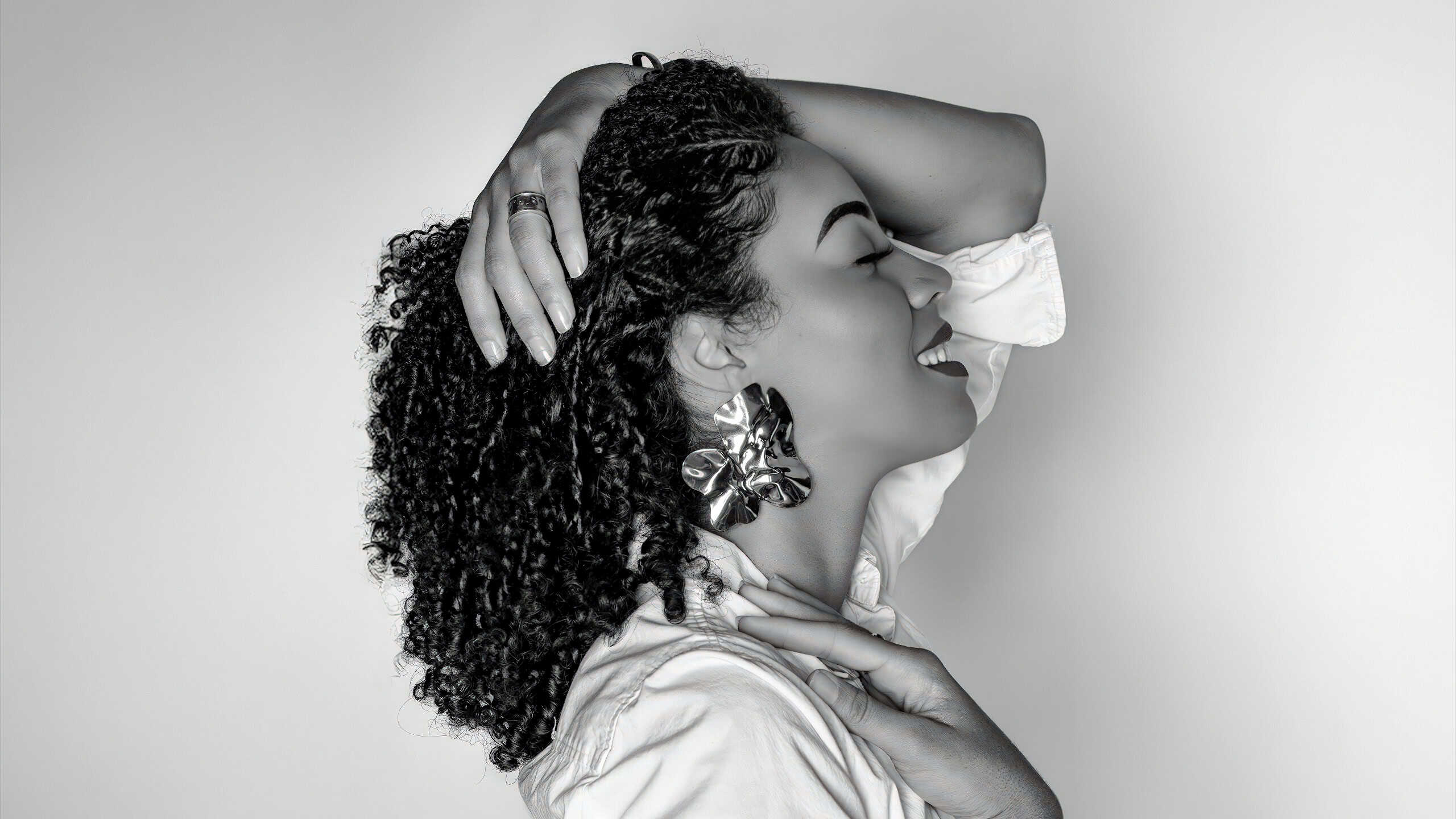Elegant woman with curly hair smiling, showcasing beauty and confidence in a black-and-white portrai.