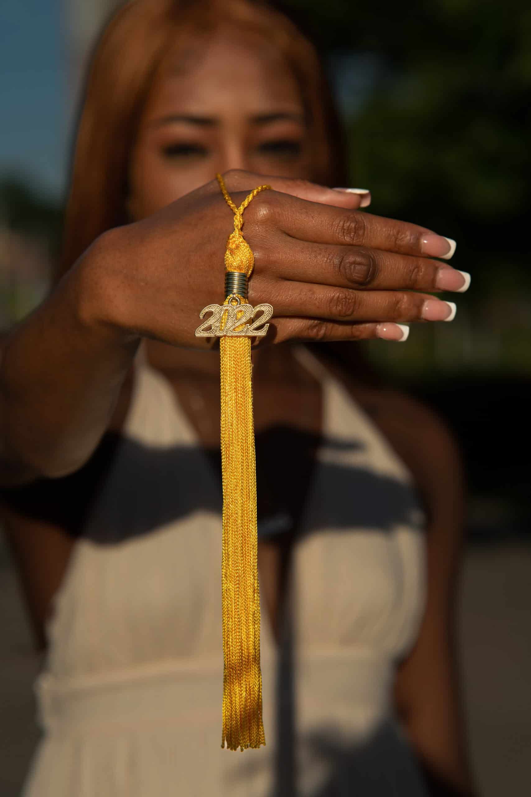 Graduation tassel with "2022" charm held by a woman outdoors.