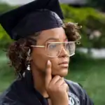 Elegant young woman in graduation cap and gown, outdoors, thoughtful pose, celebrating academic achi.