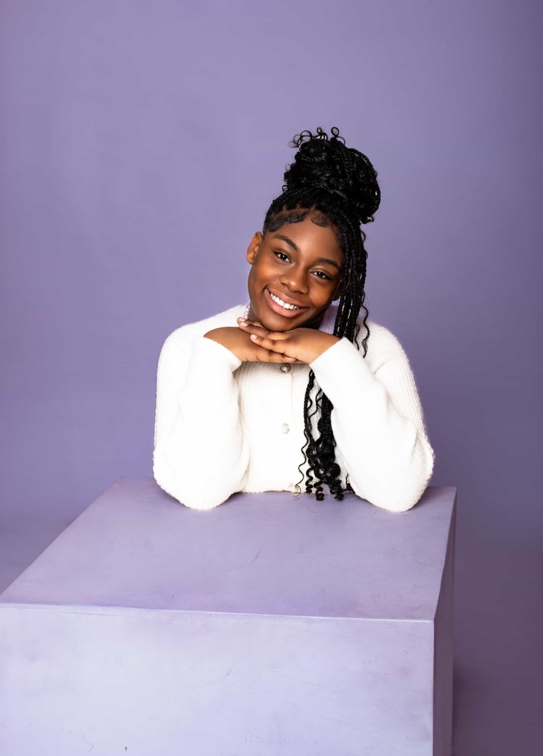 Happy woman with braided hair and a bright smile, posing against a purple background.