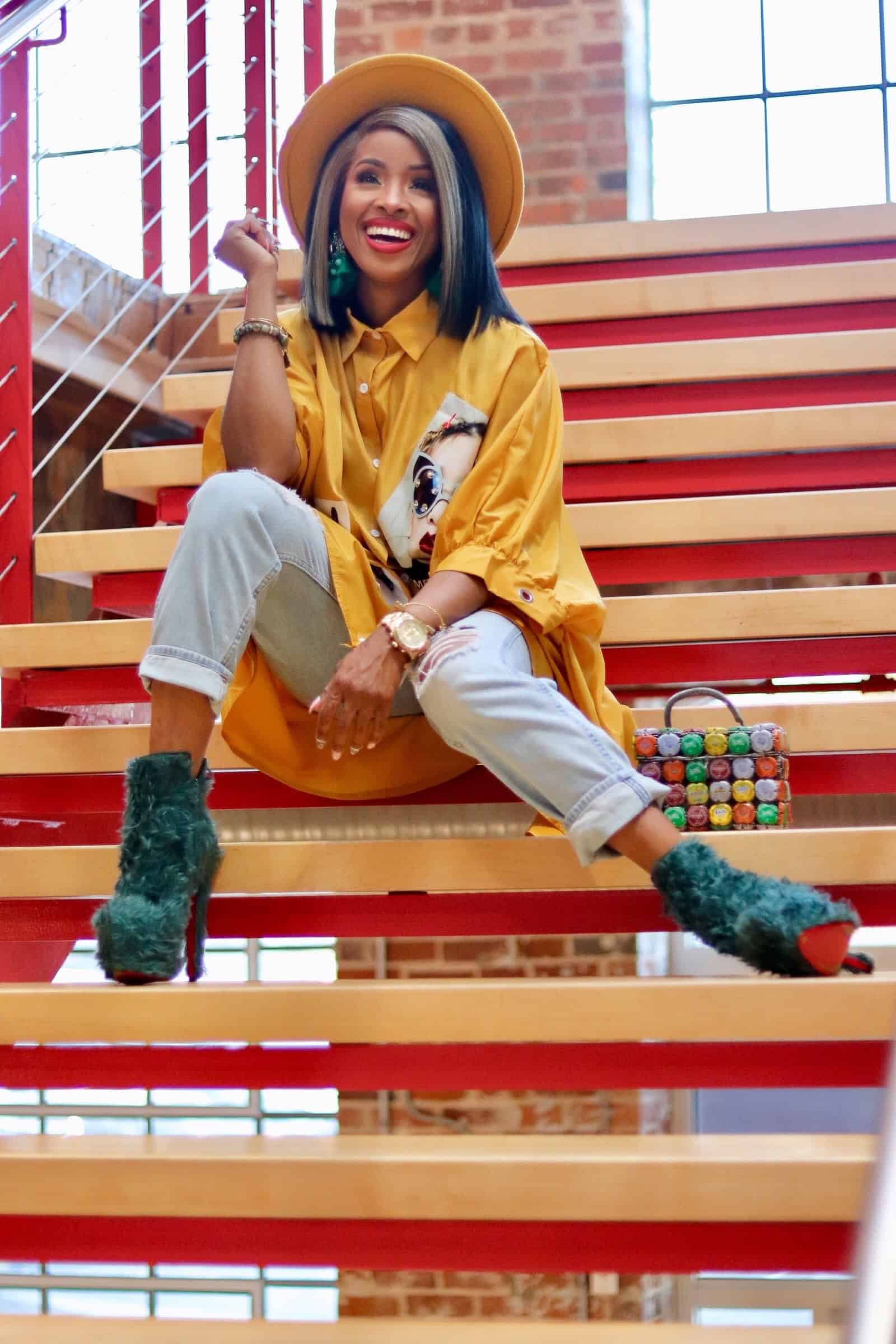 Young woman with colorful hair and bright yellow outfit sitting on stylish wooden stairs, smiling co.