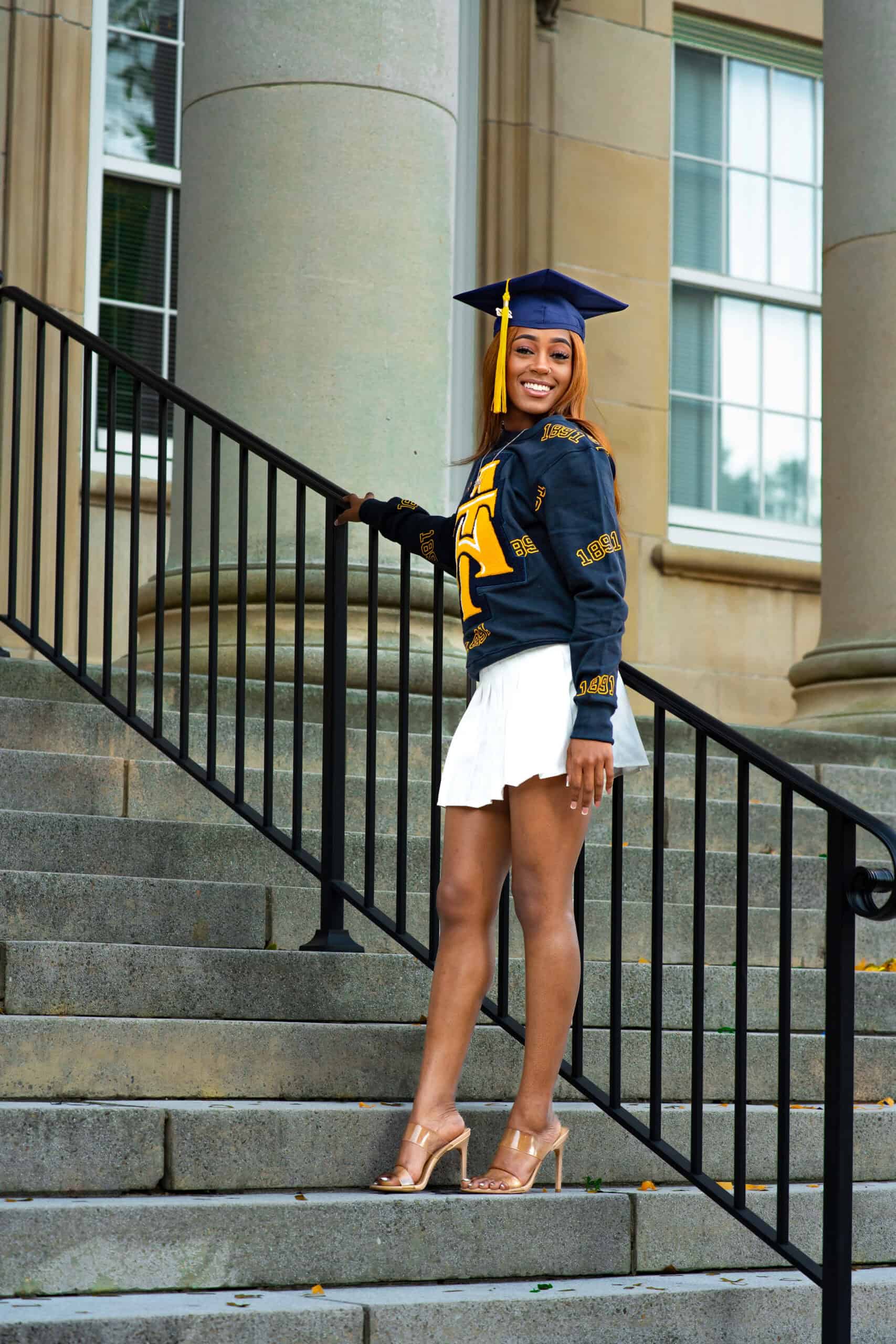 Happy graduate woman in cap and gown on stairs outside building.