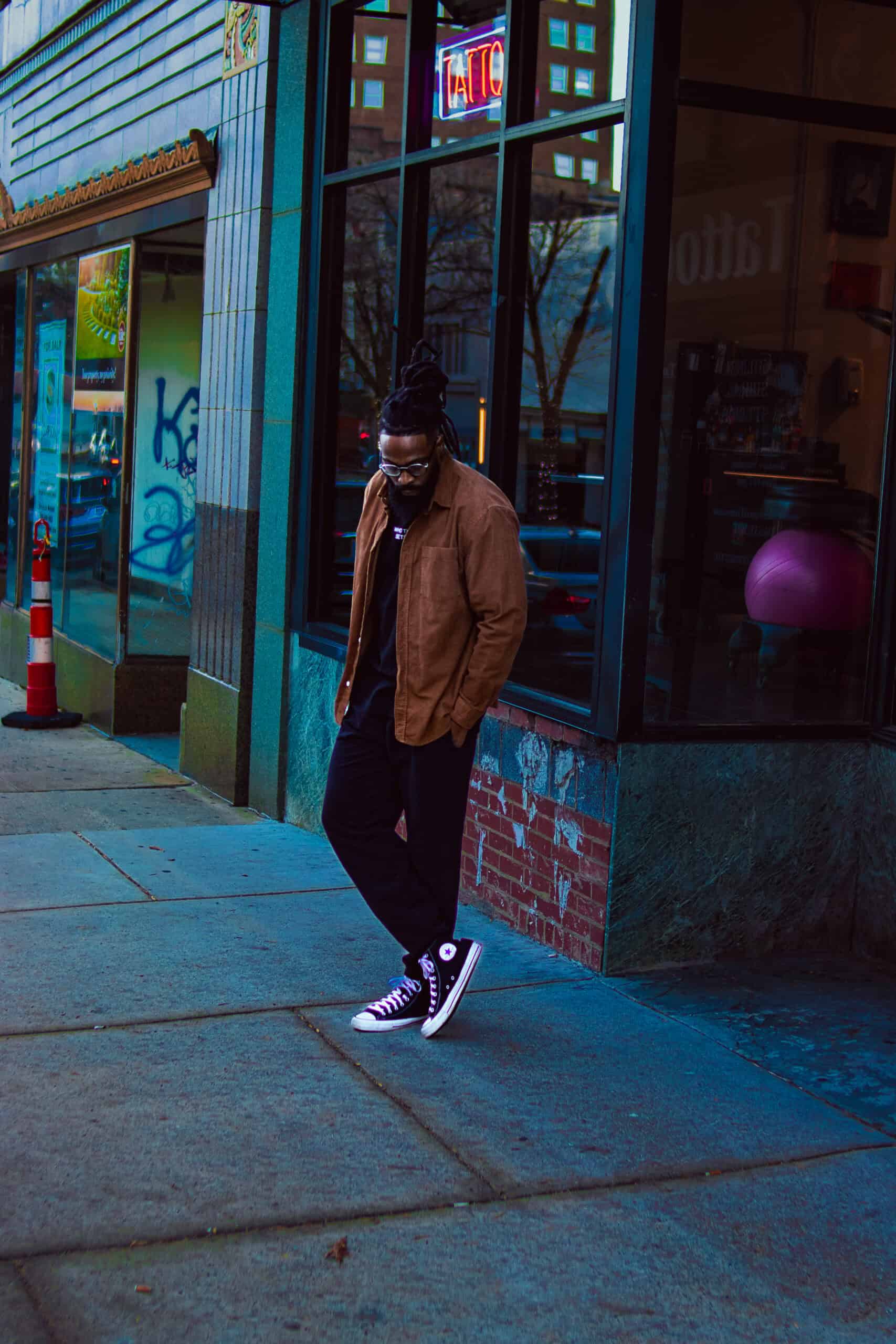 Person standing outside a storefront on a city sidewalk, wearing casual clothing and sneakers.