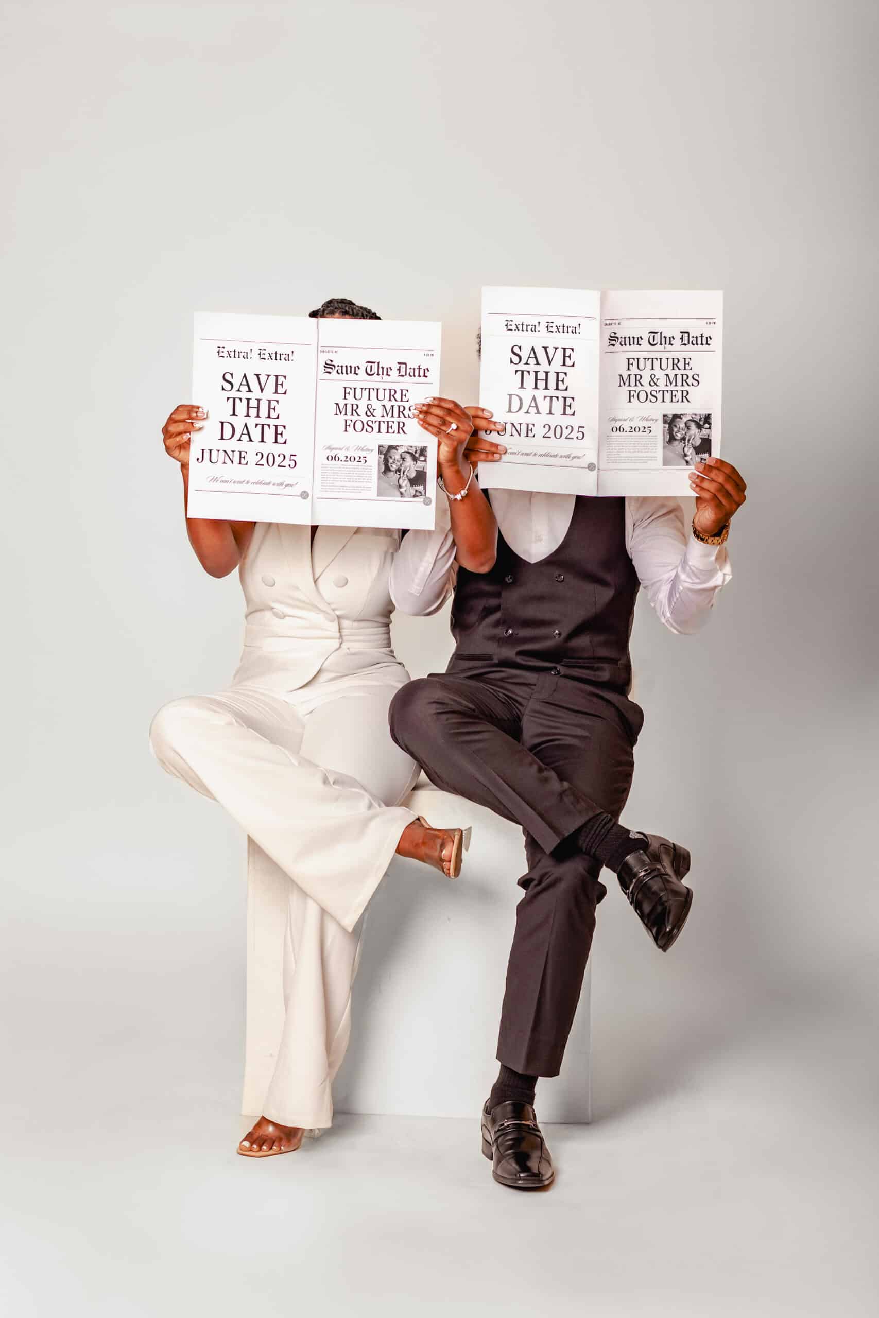 Two people in formal attire holding "Save the Date" cards, sitting against a plain background.