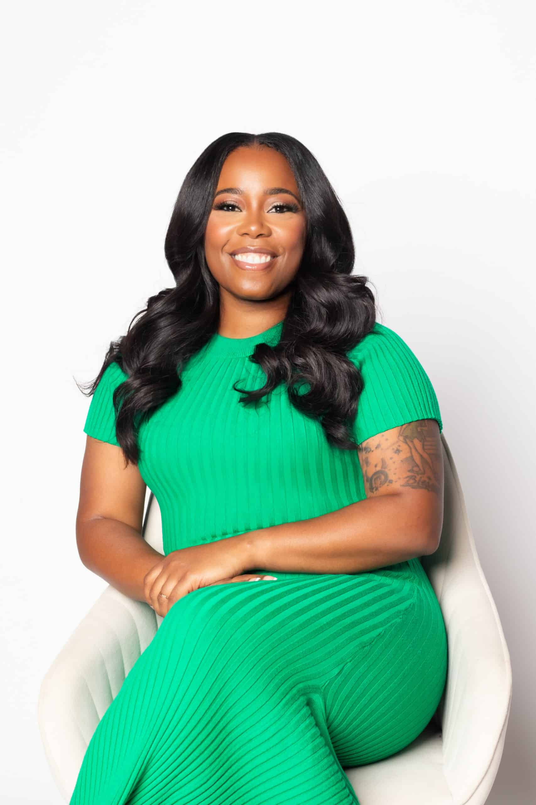 Woman in vibrant green dress smiling, sitting on white chair, Zealografy branding.