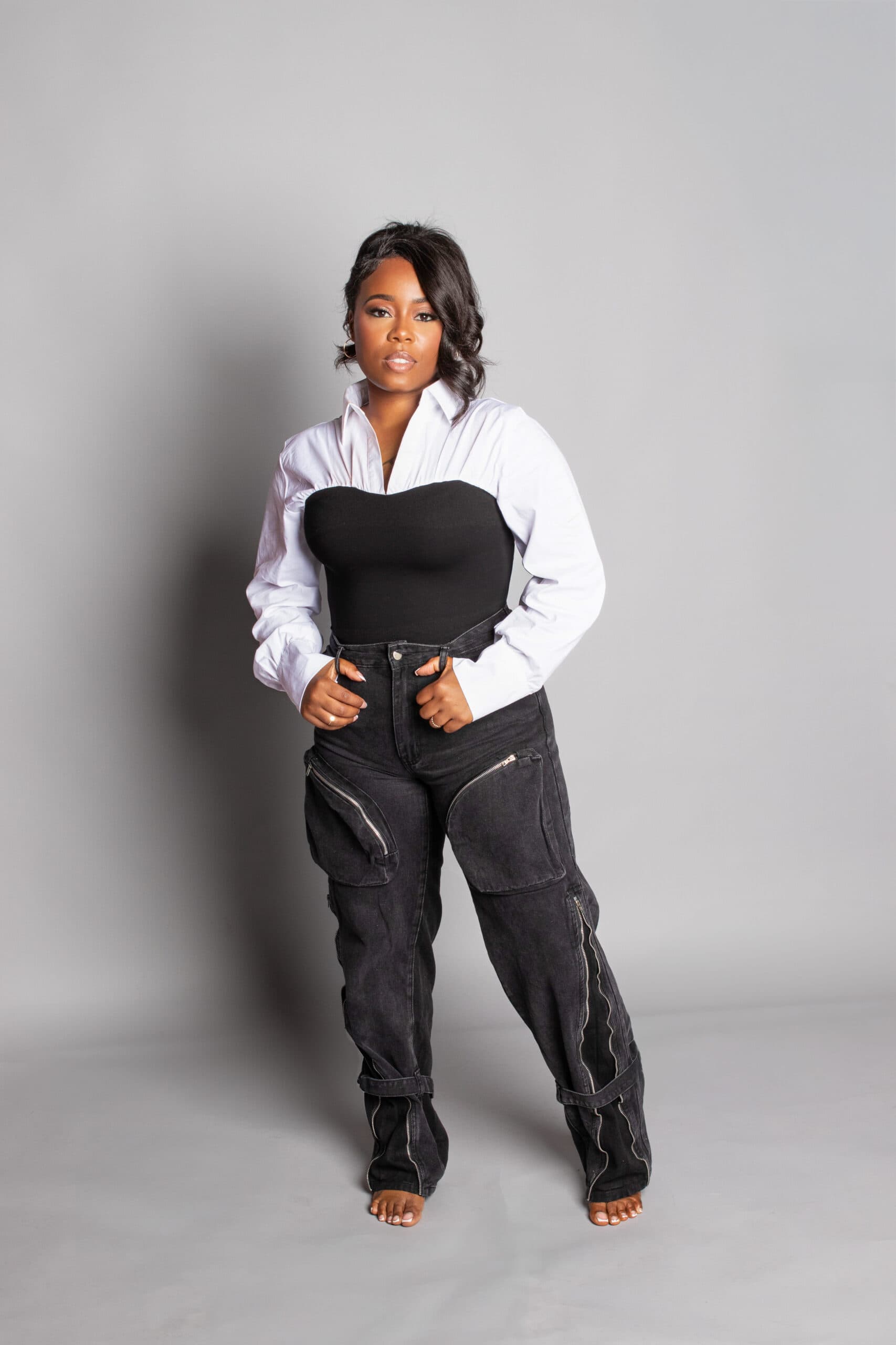 Woman wearing a white shirt and black top with black distressed jeans, standing confidently.