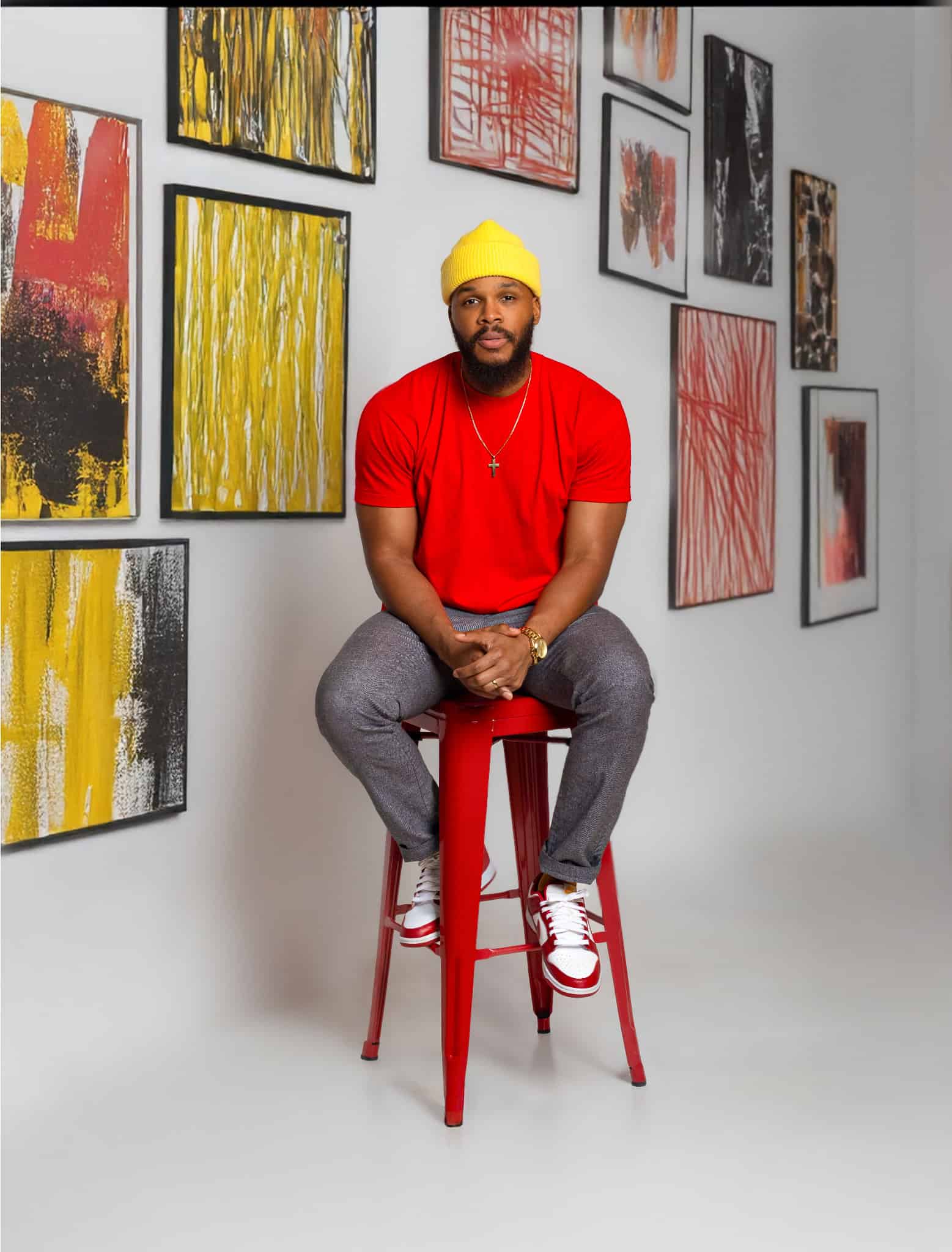African American man in red t-shirt and yellow beanie sitting on a red stool in art gallery.