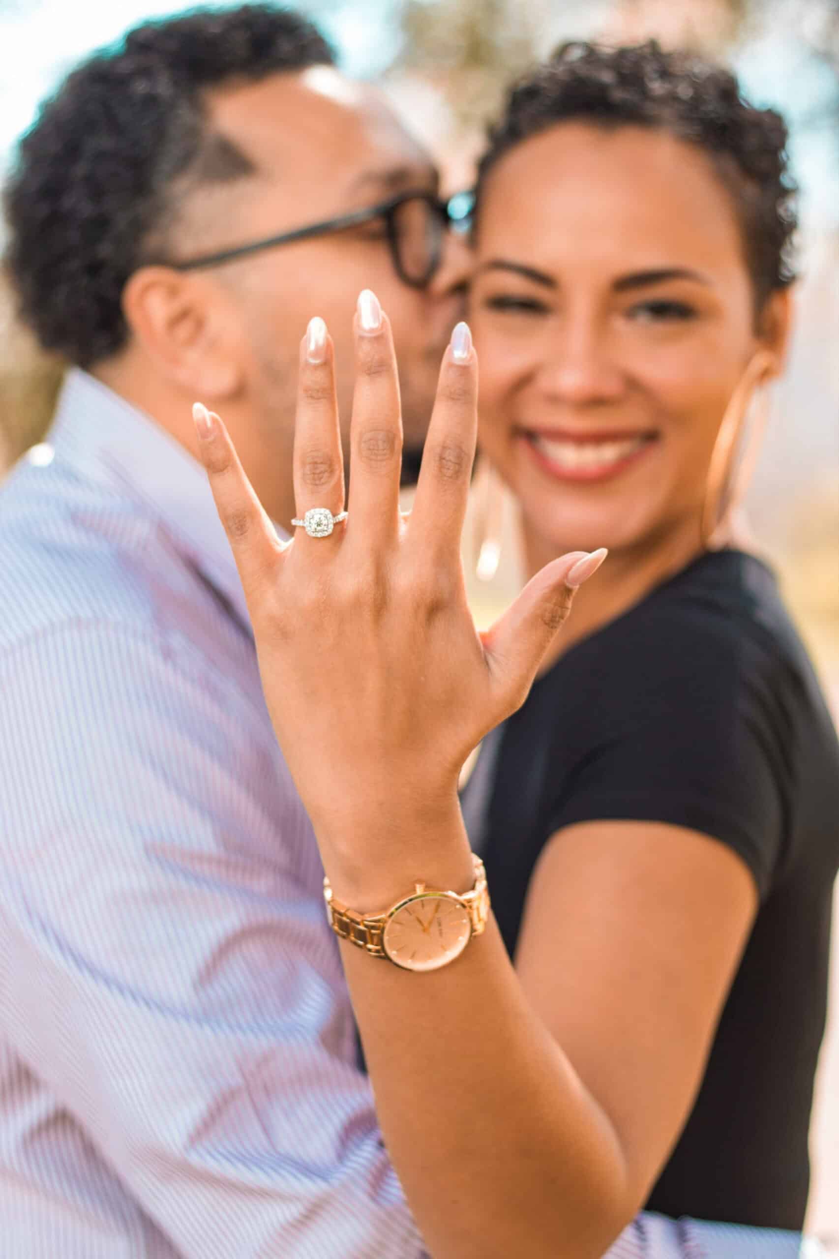 Happy woman showing her engagement ring with a joyful partner in the background.
