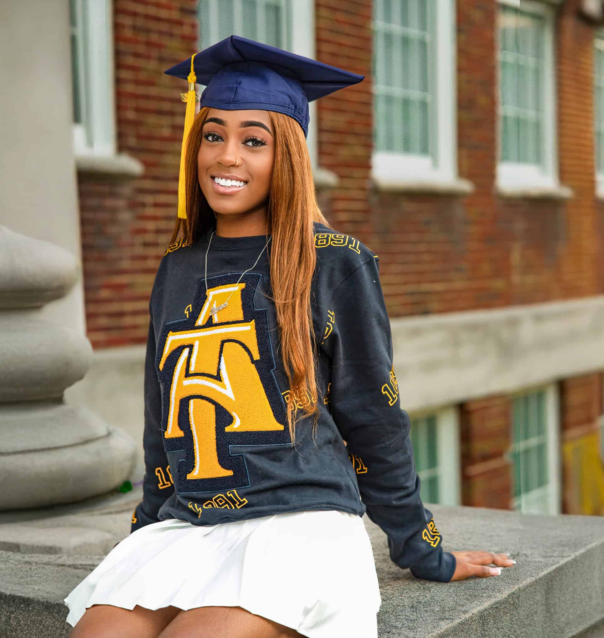 Happy graduate in cap and gown sitting outdoors, celebrating academic achievement.