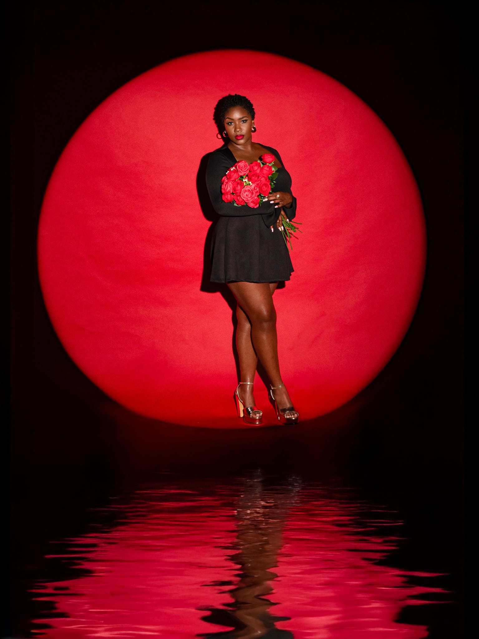 Elegant woman with roses, black dress, and high heels standing in front of a bold red circle.