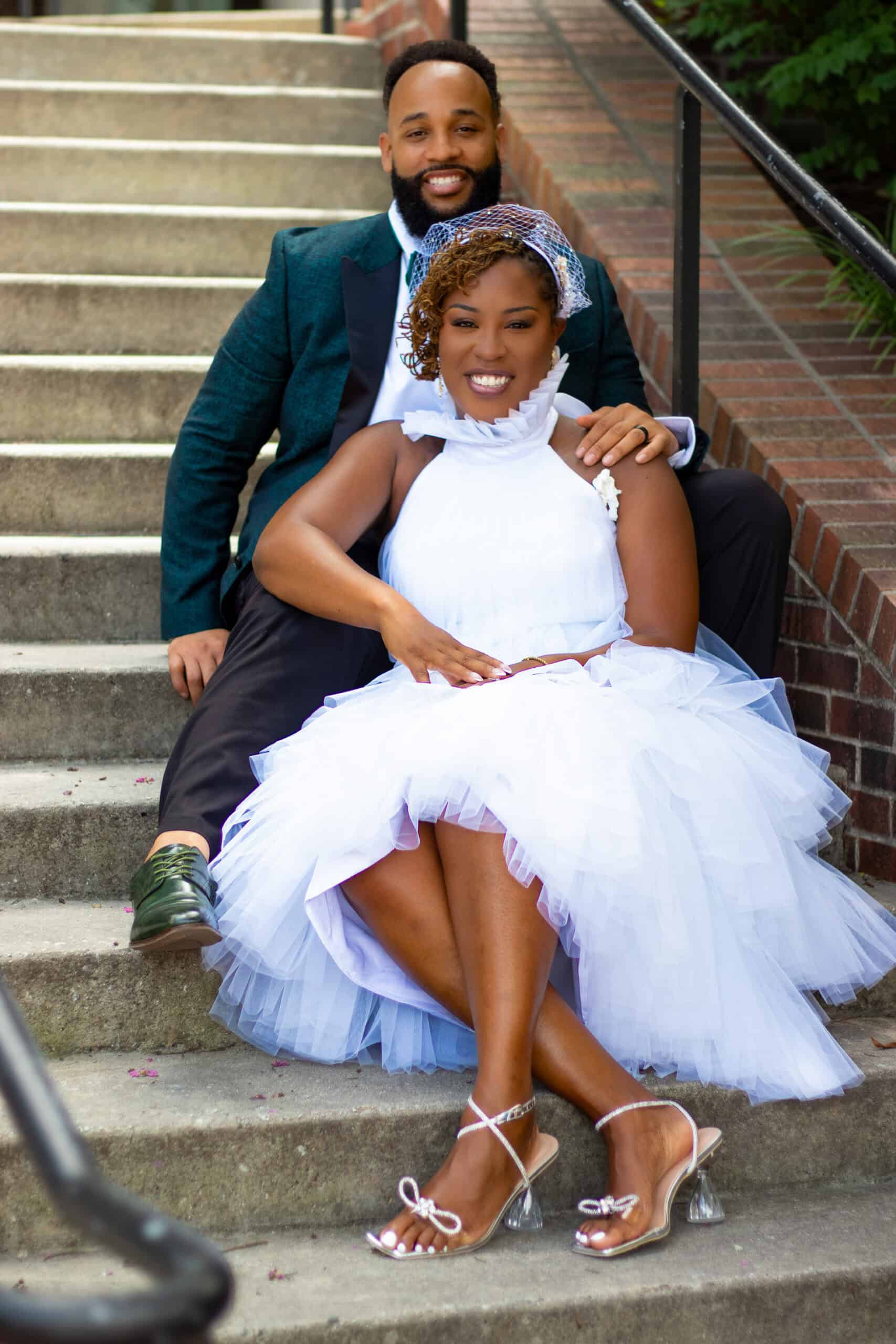 Elegant couple in wedding dress and suit sitting on outdoor stairs.