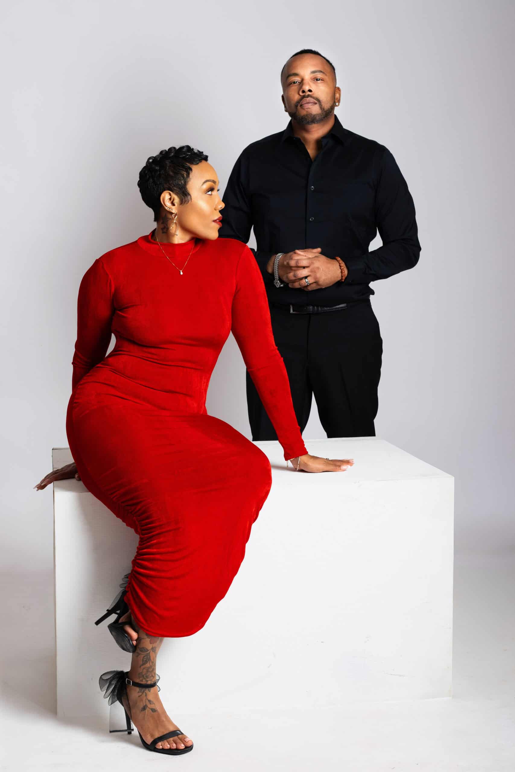 Stylish couple portrait featuring a woman in a red dress and a man in black, professional studio sho.