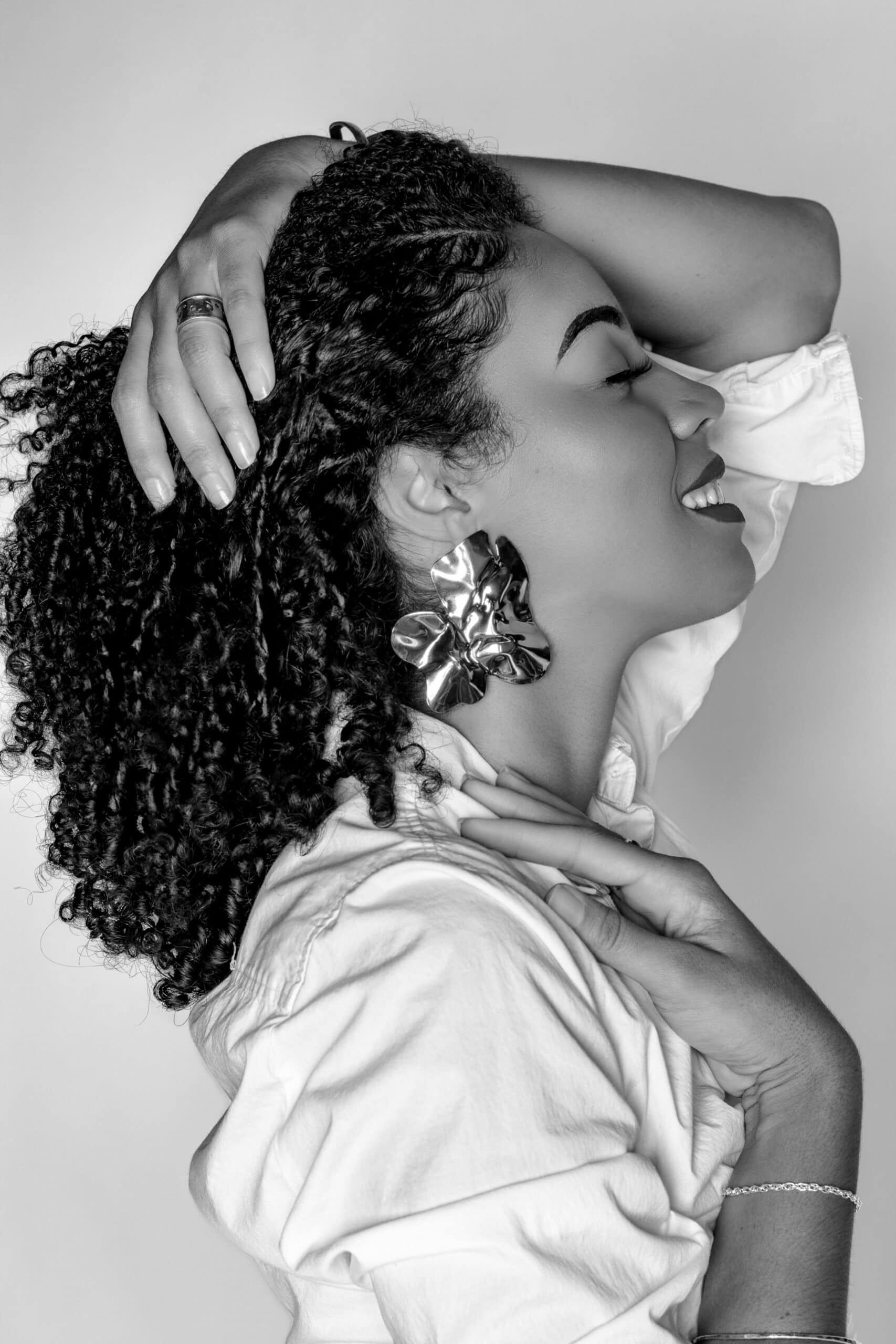 Black and white portrait of a smiling woman with curly hair and large earrings.