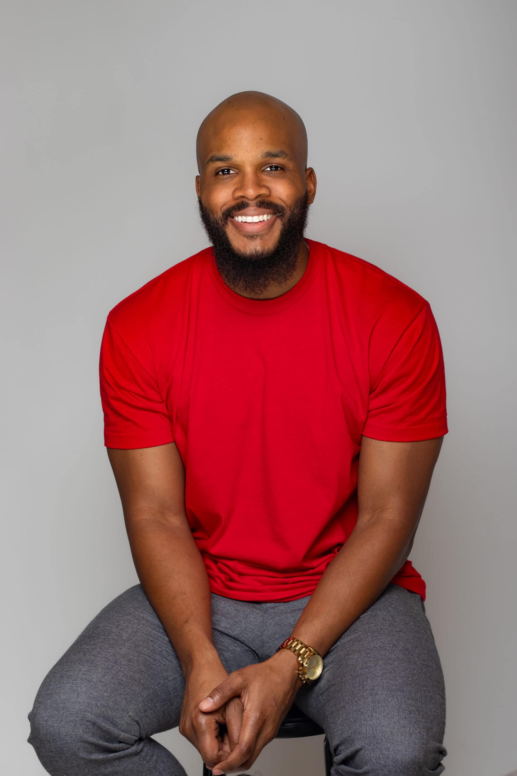 Happy man with a beard wearing a red T-shirt, sitting against a neutral background.