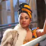 A woman with a colorful headwrap and fur stole posing on a construction site.